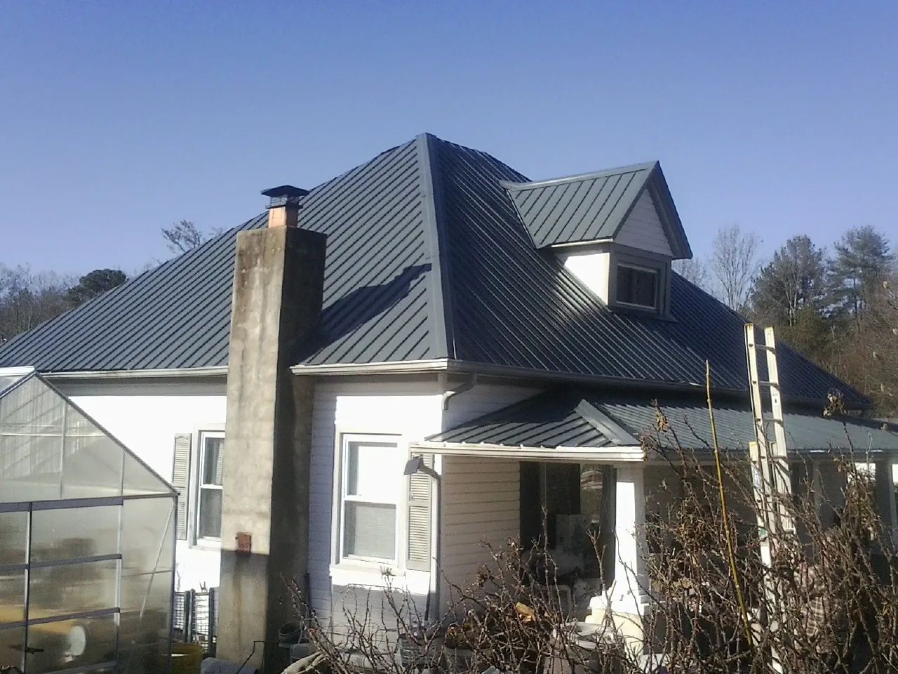 Dark blue standing seam metal roof on a white farmhouse with dormer — Slate & Tile Roof Repair by Roofing Brothers in Wittman