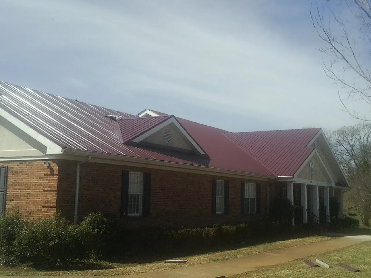 Red metal roof with gabled entries on a long brick building, from a Hail Damage Roof Repair job in Wittman