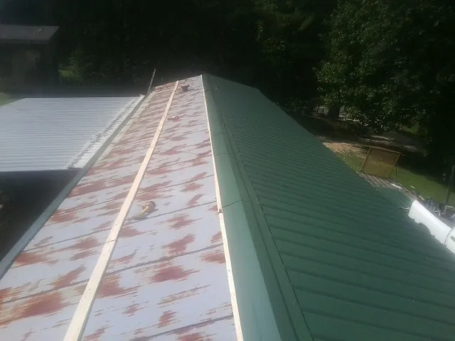 Old rusted panels beside newly installed green metal roofing — Wind Damage Roof Repair by Roofing Brothers in Wittman
