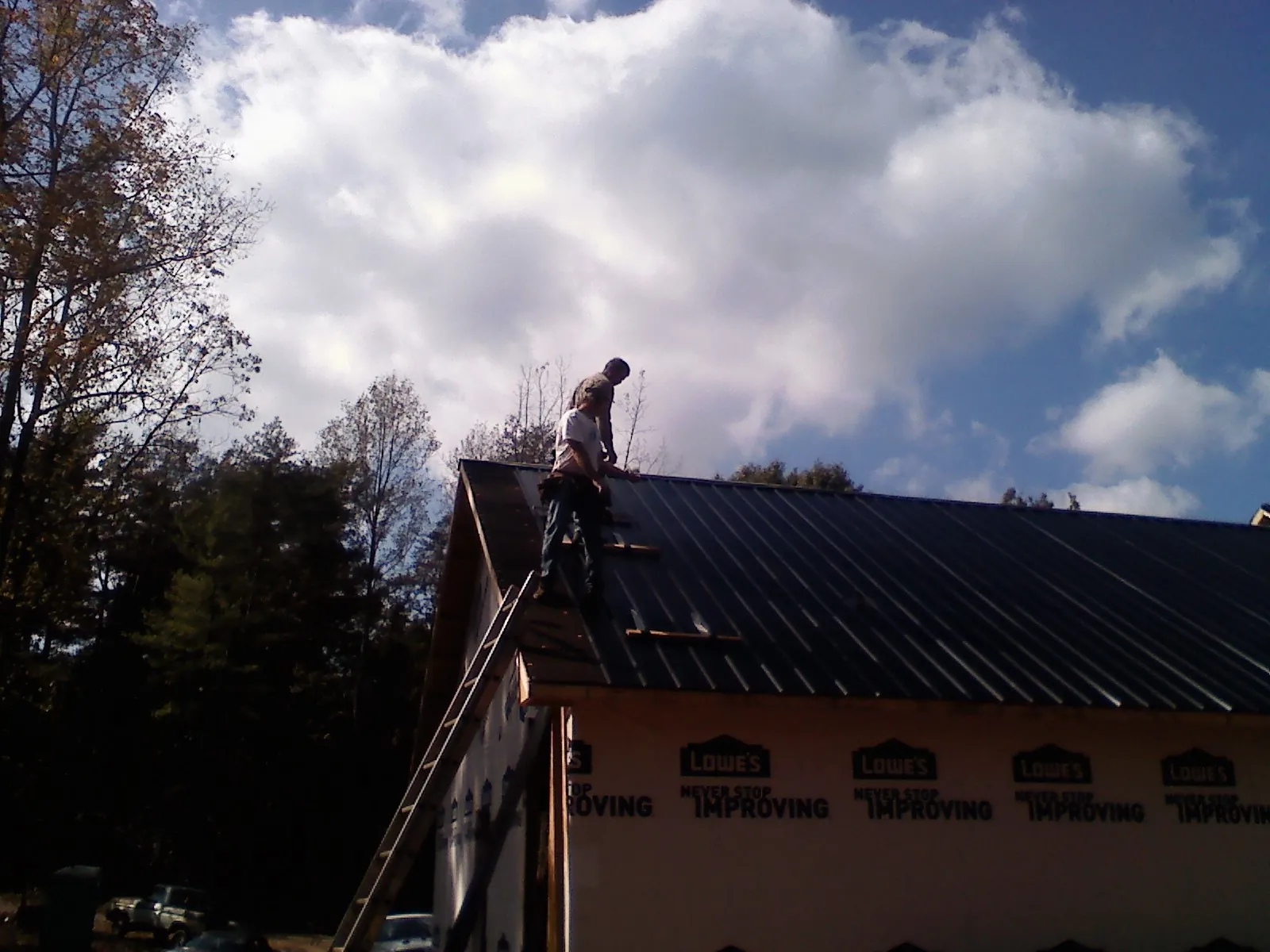 Roofer fastening dark metal panels high against a cloudy sky, from a Roof Inspection job in Wittman